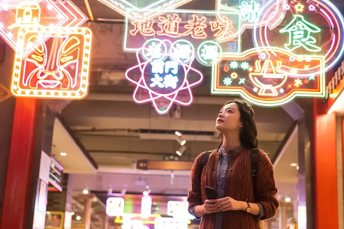 Young woman exploring an indoor street filled with colorful neon signs in Chinese characters