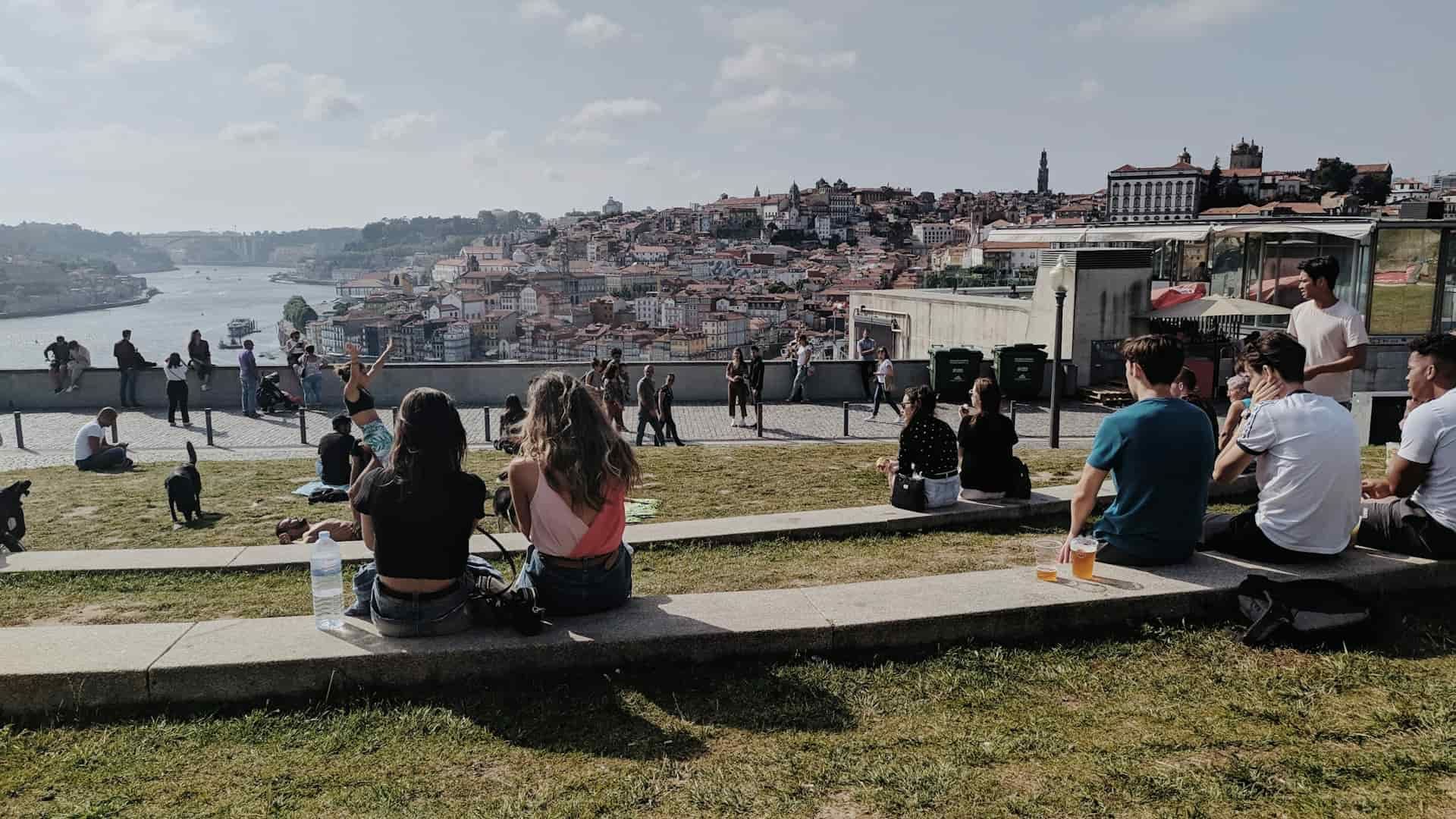 Group of young travelers relaxing on a grassy viewpoint overlooking a scenic European cityscape and river