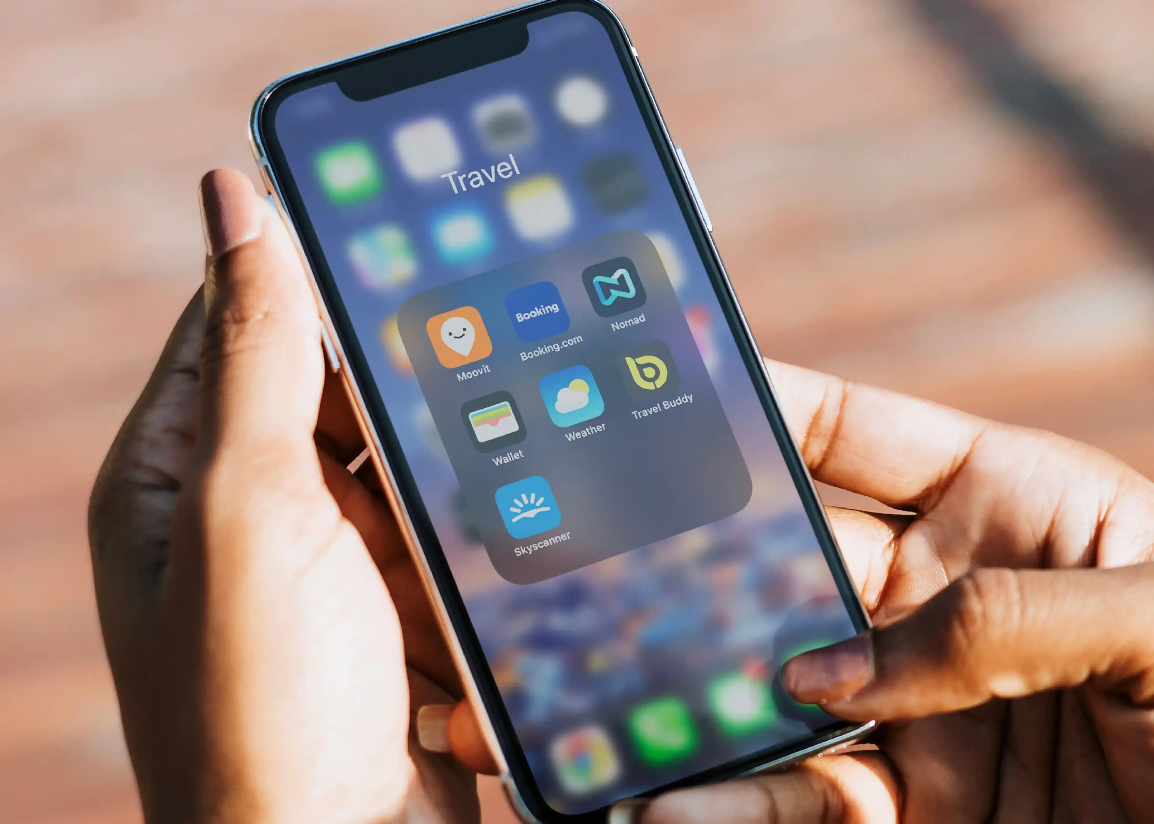 Top 10 travel apps for 2023: A close-up of a smartphone showing essential travel apps like Nomad and Booking.com organized in a folder for easy trip planning.