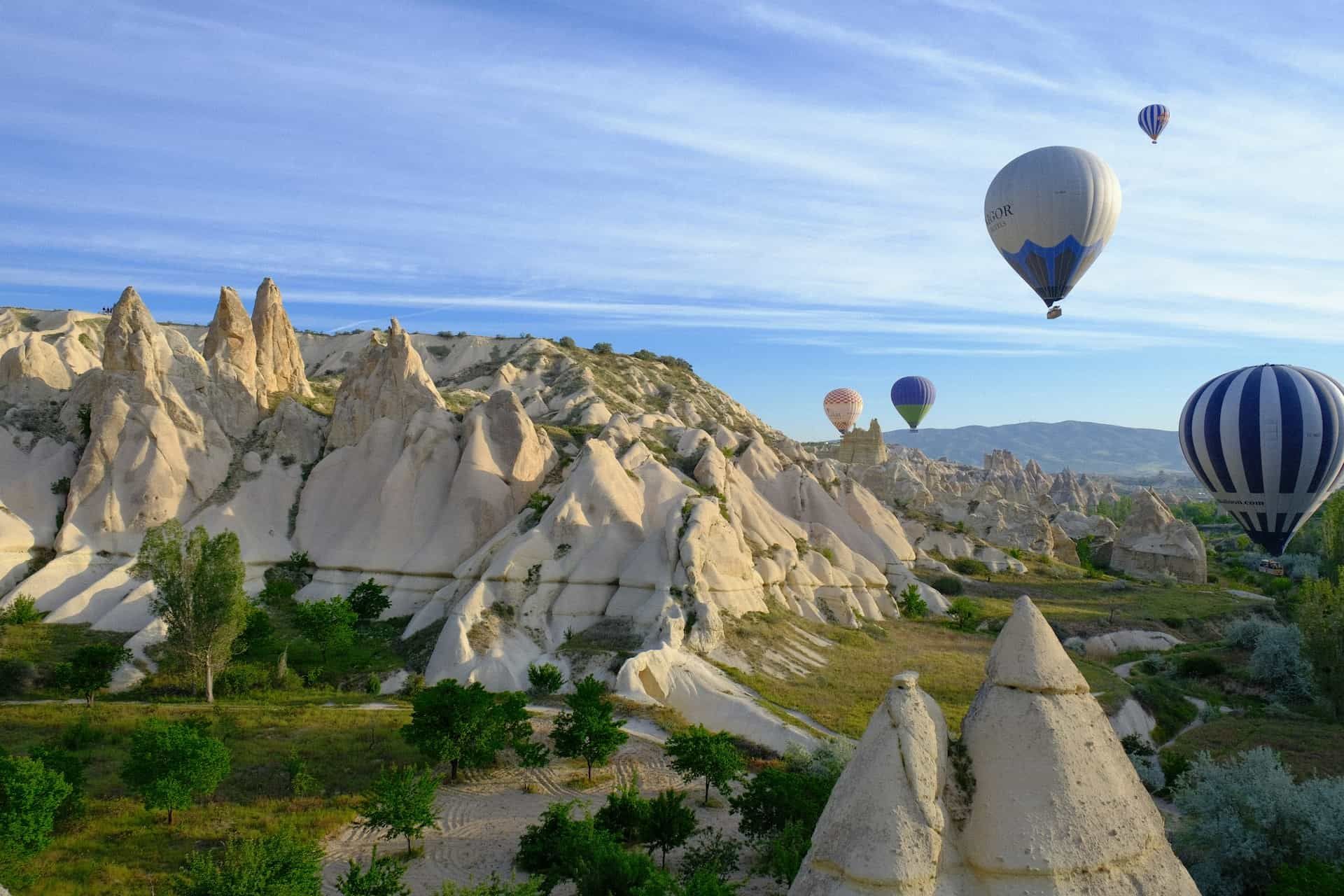 Hot air balloons floating over unique rock formations and fairy chimneys in Cappadocia, Turkey under a clear blue sky.