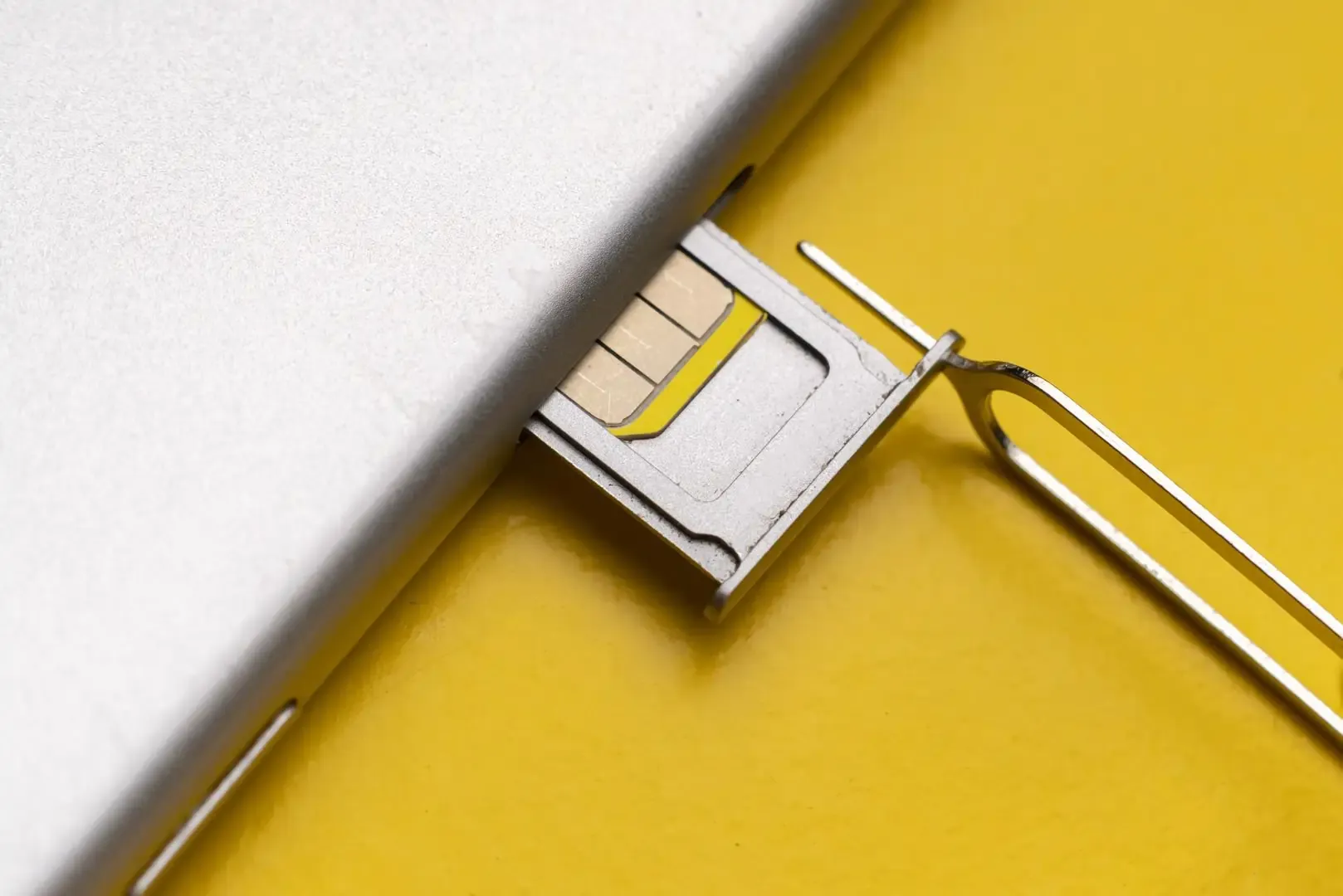 Close up of a SIM card tray partially ejected from a phone with a SIM removal tool inserted