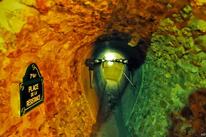 Narrow underground tunnel of the Paris Sewer Museum with stone walls and a vintage street sign reading “Place de la Résistance”.