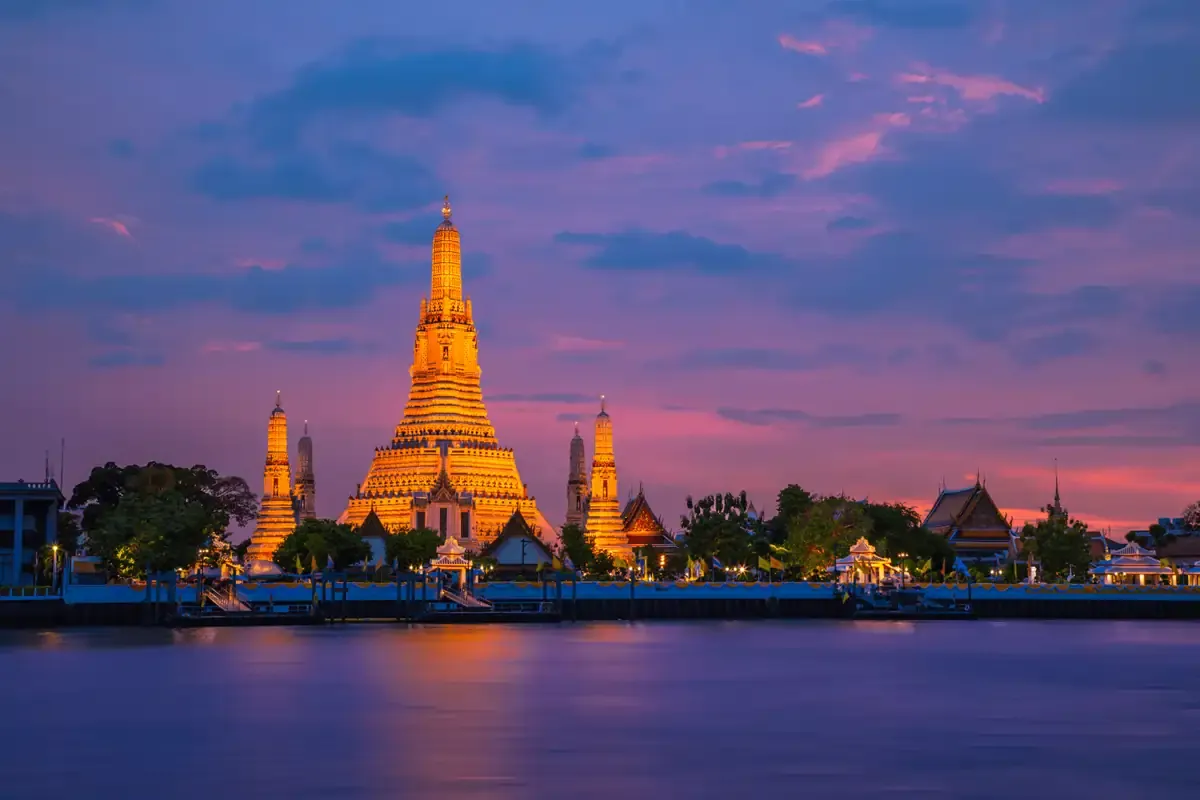 Wat Arun temple illuminated at sunset along the Chao Phraya River in Bangkok.