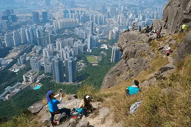 Hikers on Lion Rock trail overlooking dense skyscrapers and cityscape of Hong Kong on a clear day