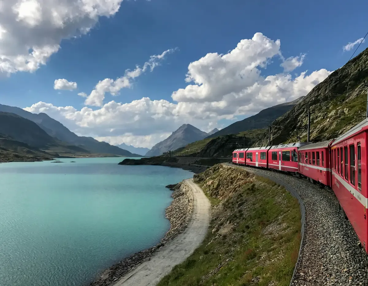 Scenic train travelling through the Swiss Alps alongside a mountain lake.