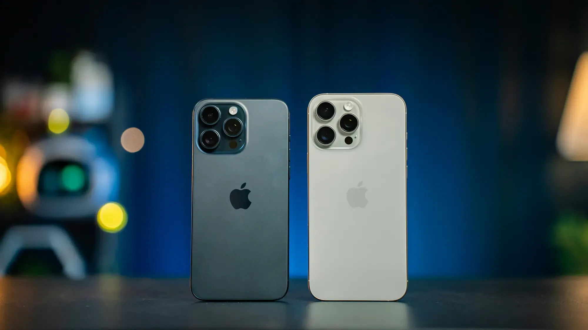 Rear view of two Apple iPhone Pro models standing side by side, comparing the triple camera system and different color finishes.