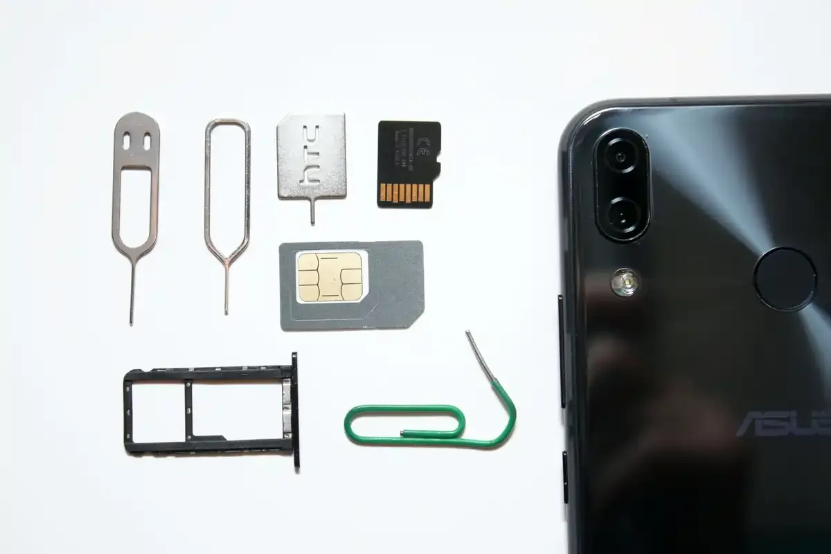 Various SIM tools, card tray, SIM, and phone laid out on a white surface.