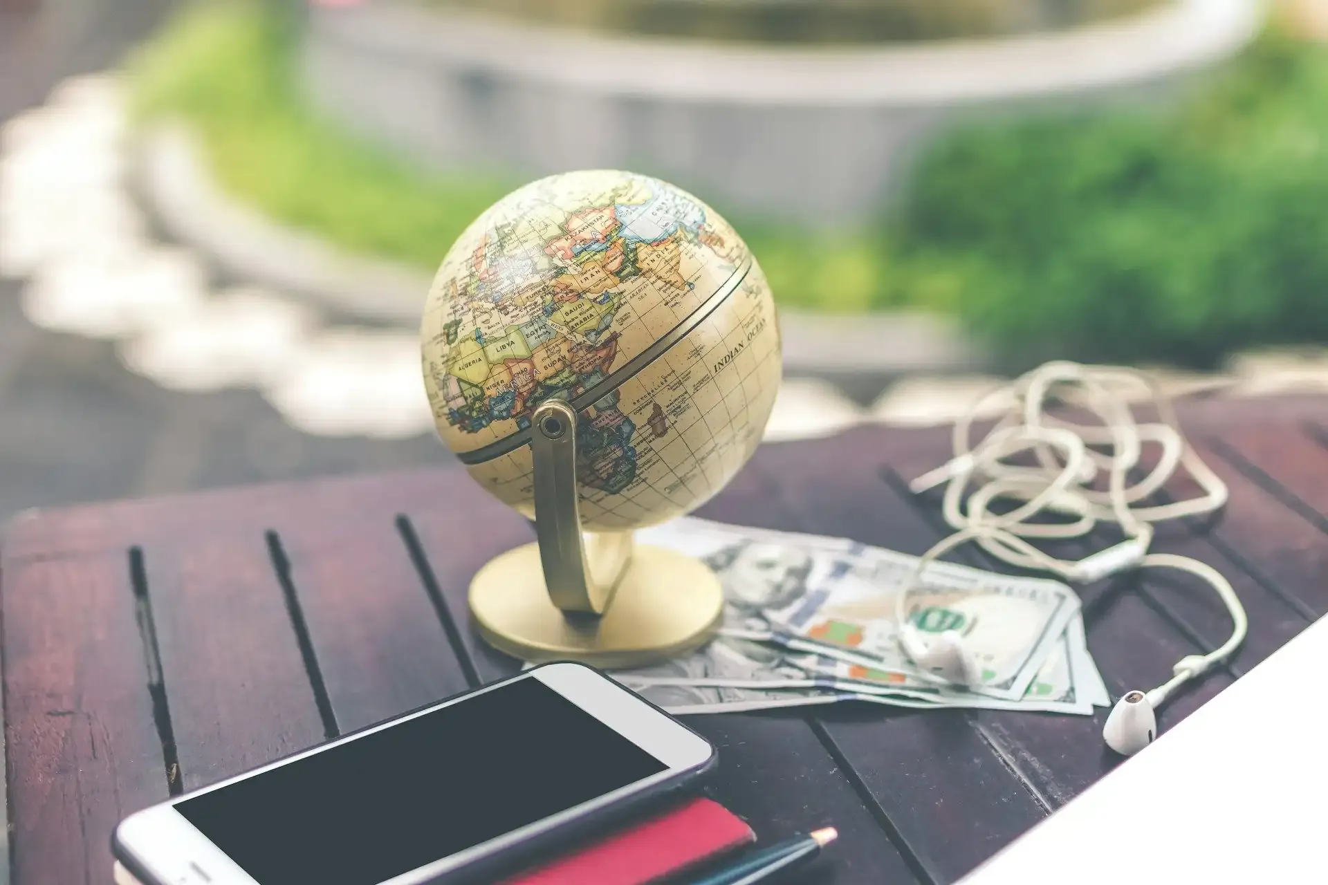 Travel essentials on a table including globe, phone, cash, and earphones—planning for internet outages abroad