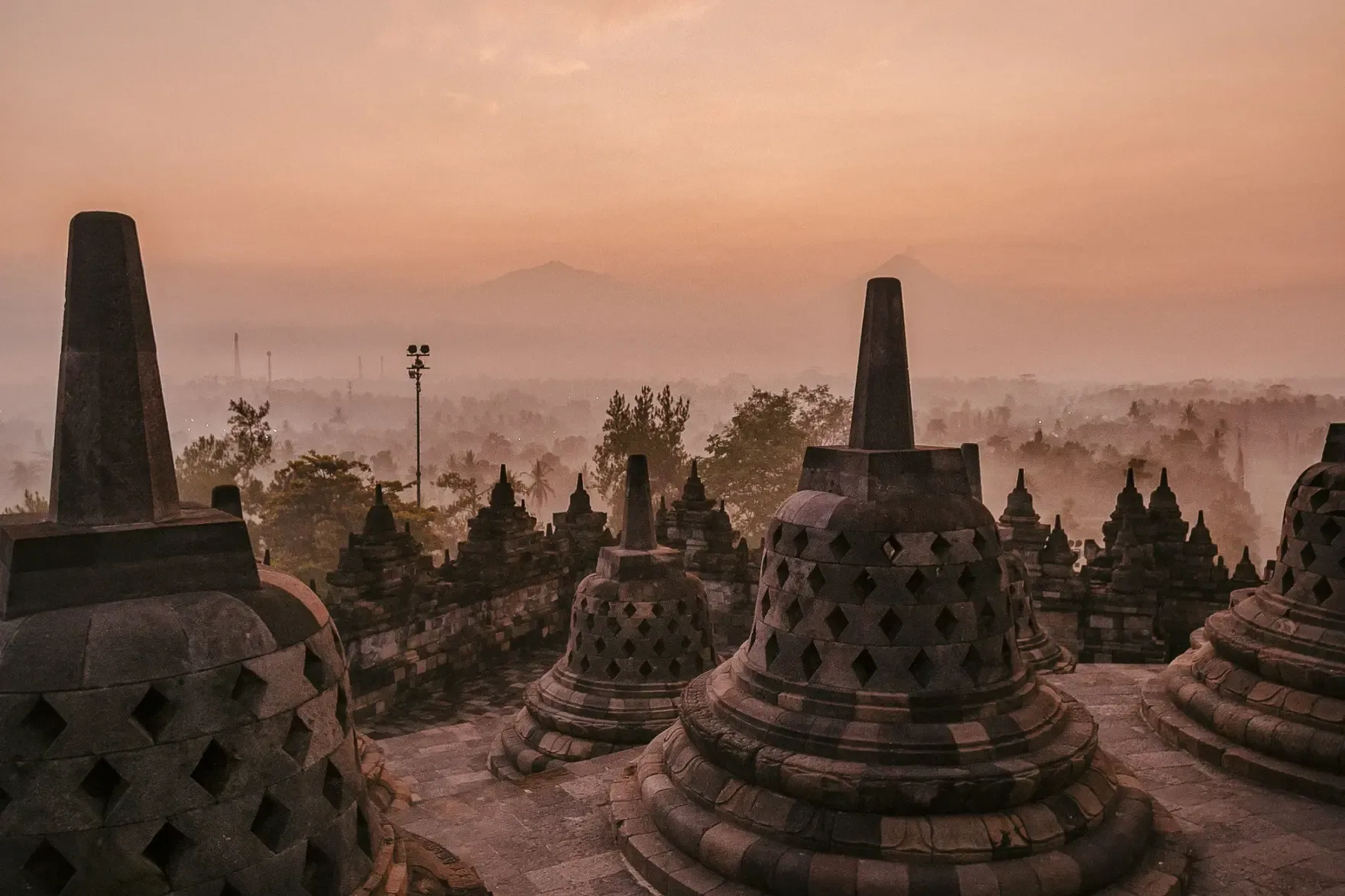 Borobudur Temple stupas overlooking a misty landscape at sunrise.