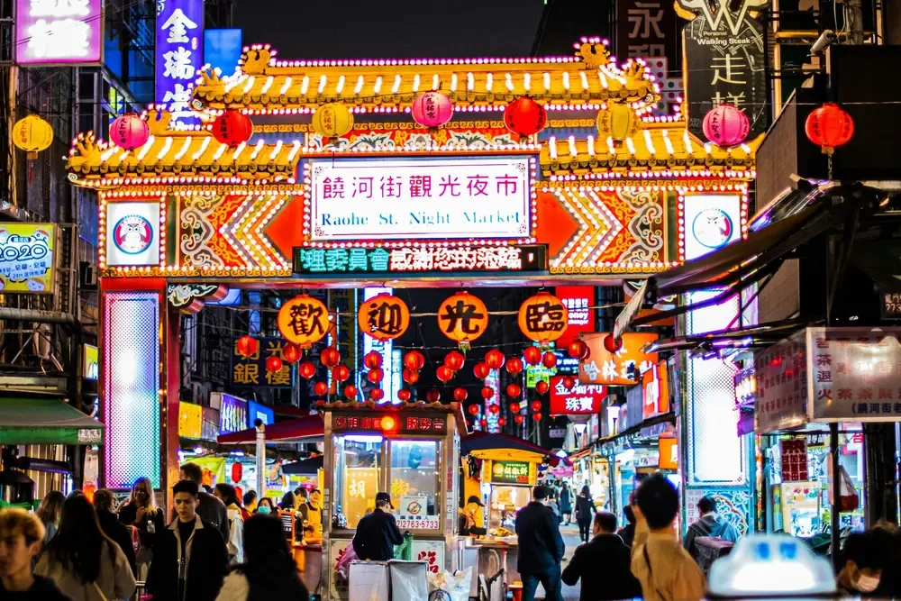 Illuminated entrance to Raohe Street Night Market in Taipei, surrounded by red lanterns and food stalls.