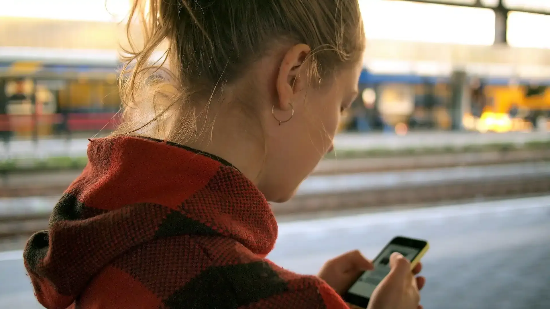 Woman at a train station platform checking her smartphone to monitor roaming data usage while traveling