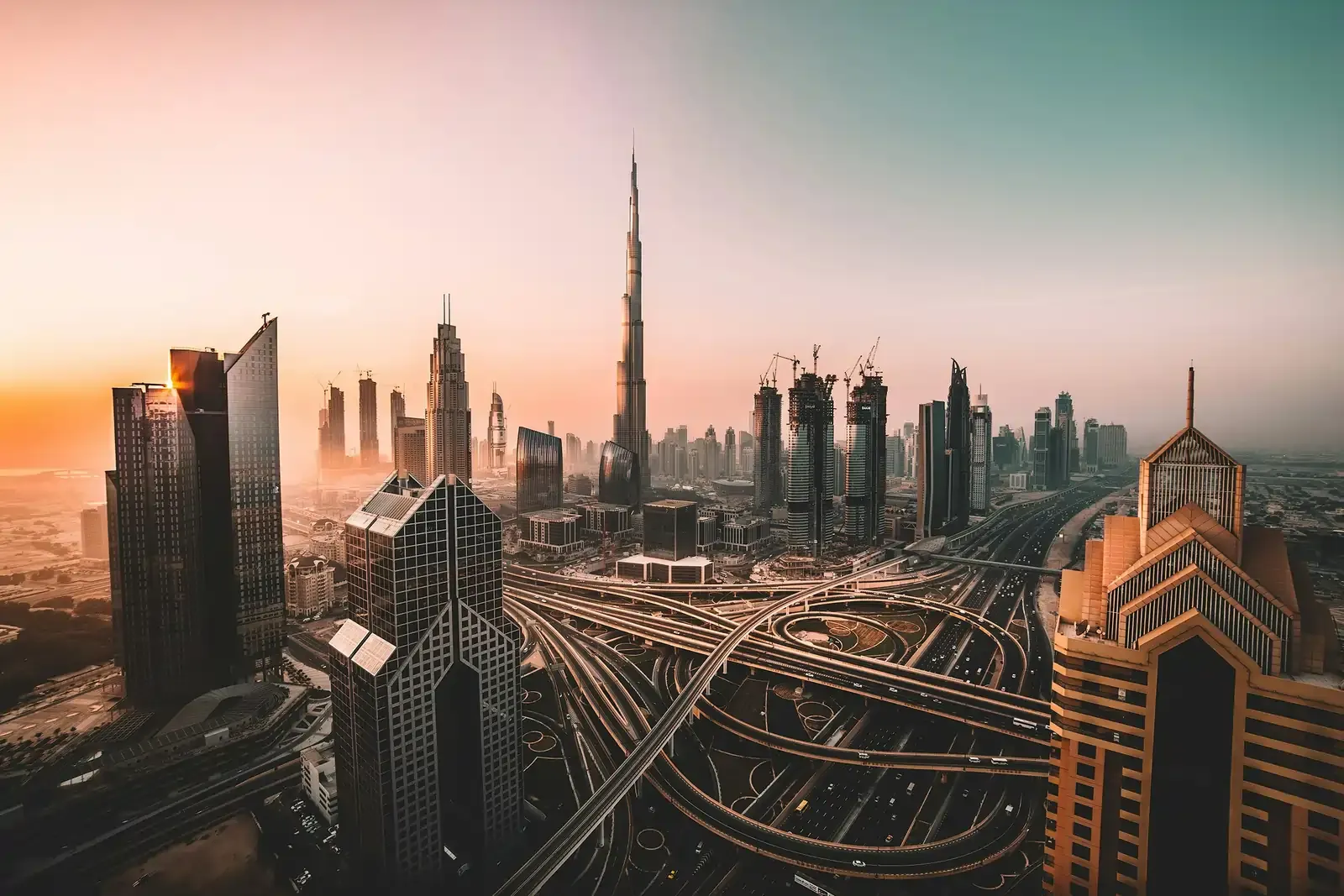 Dubai skyline at sunset featuring the Burj Khalifa and multilayered highway interchanges below.