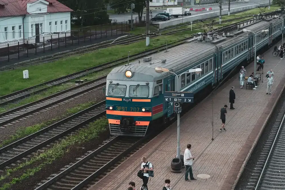 Passengers walking along the platform beside a teal and orange European train at a railway station.