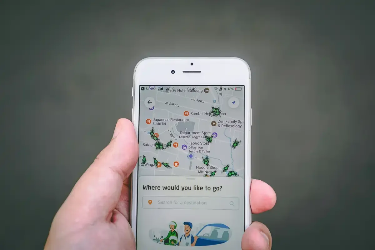 Close-up of a person holding a smartphone displaying a ridesharing app map with available drivers in Southeast Asia.