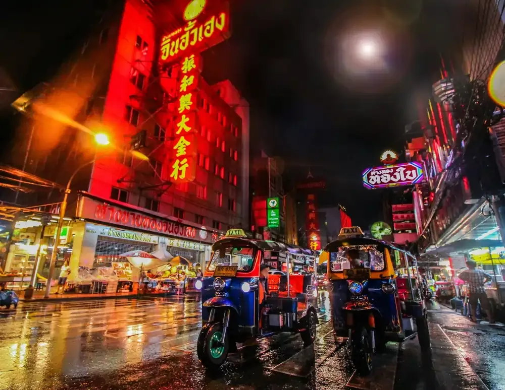 Vibrant night scene in Bangkok’s Chinatown, with tuk-tuks lined up under glowing neon signs and red-lit buildings