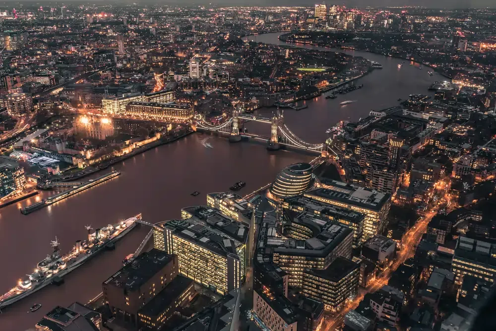 Aerial night view of London with the River Thames winding through the city and Tower Bridge illuminated.