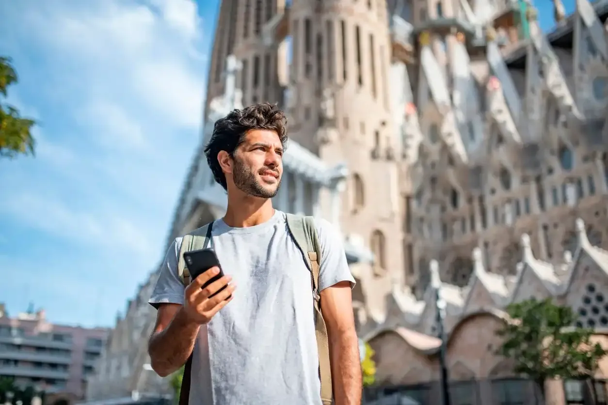 Smiling tourist in Barcelona using smartphone in front of Sagrada Família.