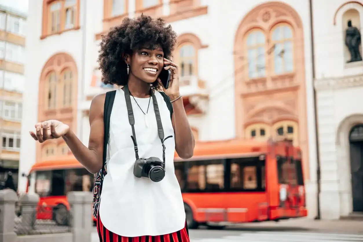 Happy tourist on a phone call while sightseeing, with camera around neck and city bus in background