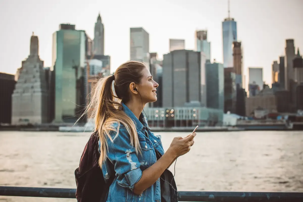 Female tourist using mobile phone with eSIM while exploring New York City skyline