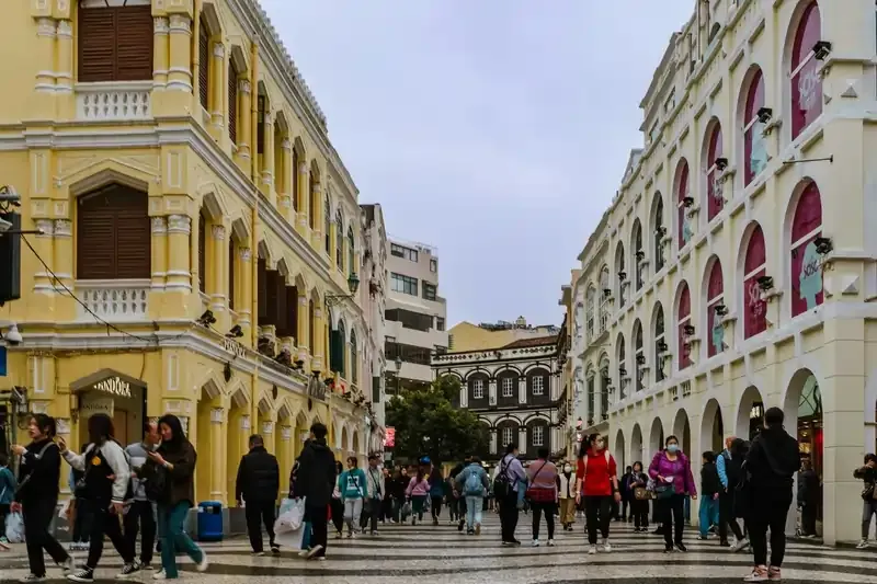 People exploring Macau’s heritage district at Senado Square, framed by pastel-colored colonial buildings and patterned cobblestones.