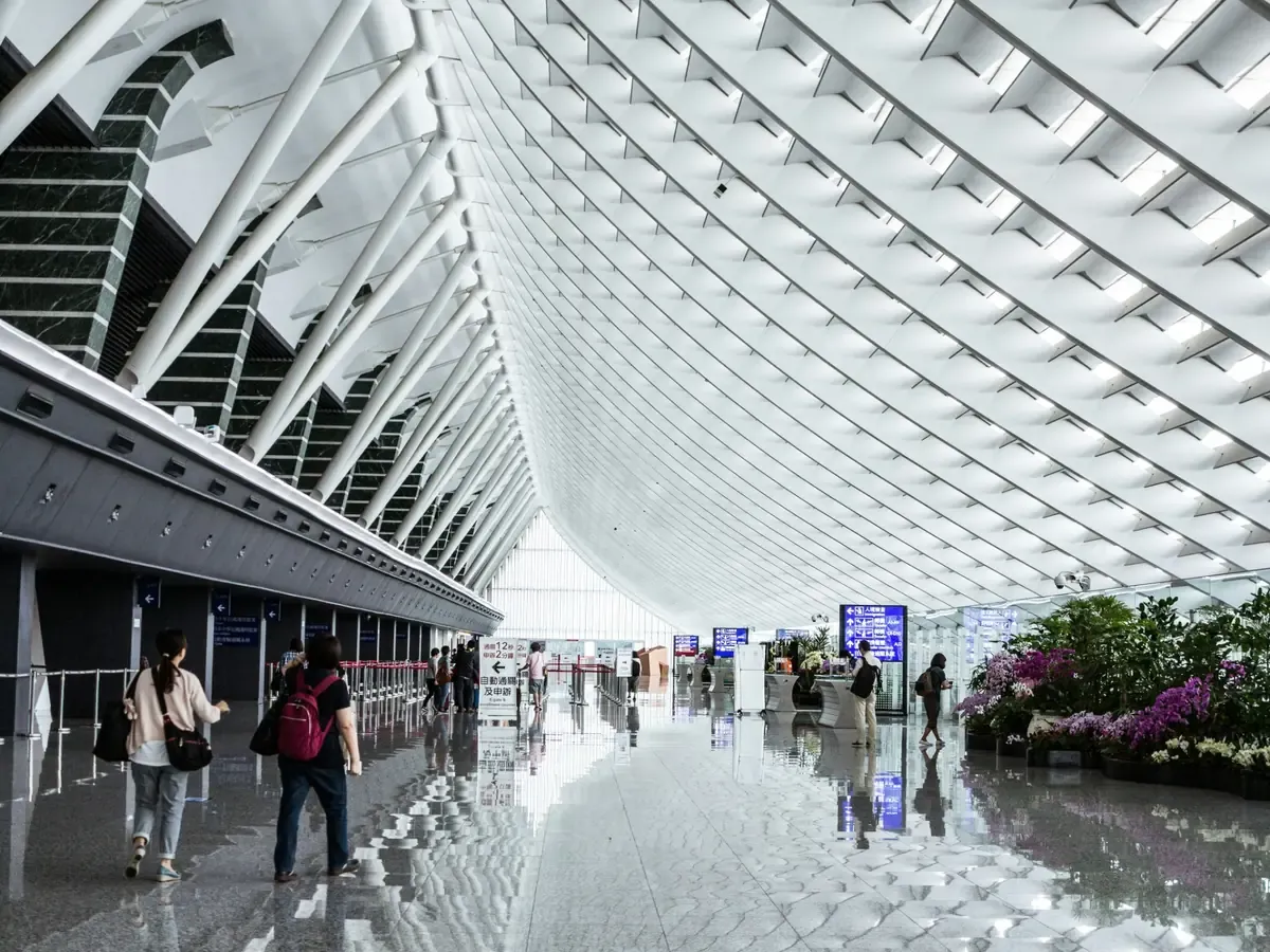 Travellers walking through a bright Taiwan airport terminal with a curved white roof.