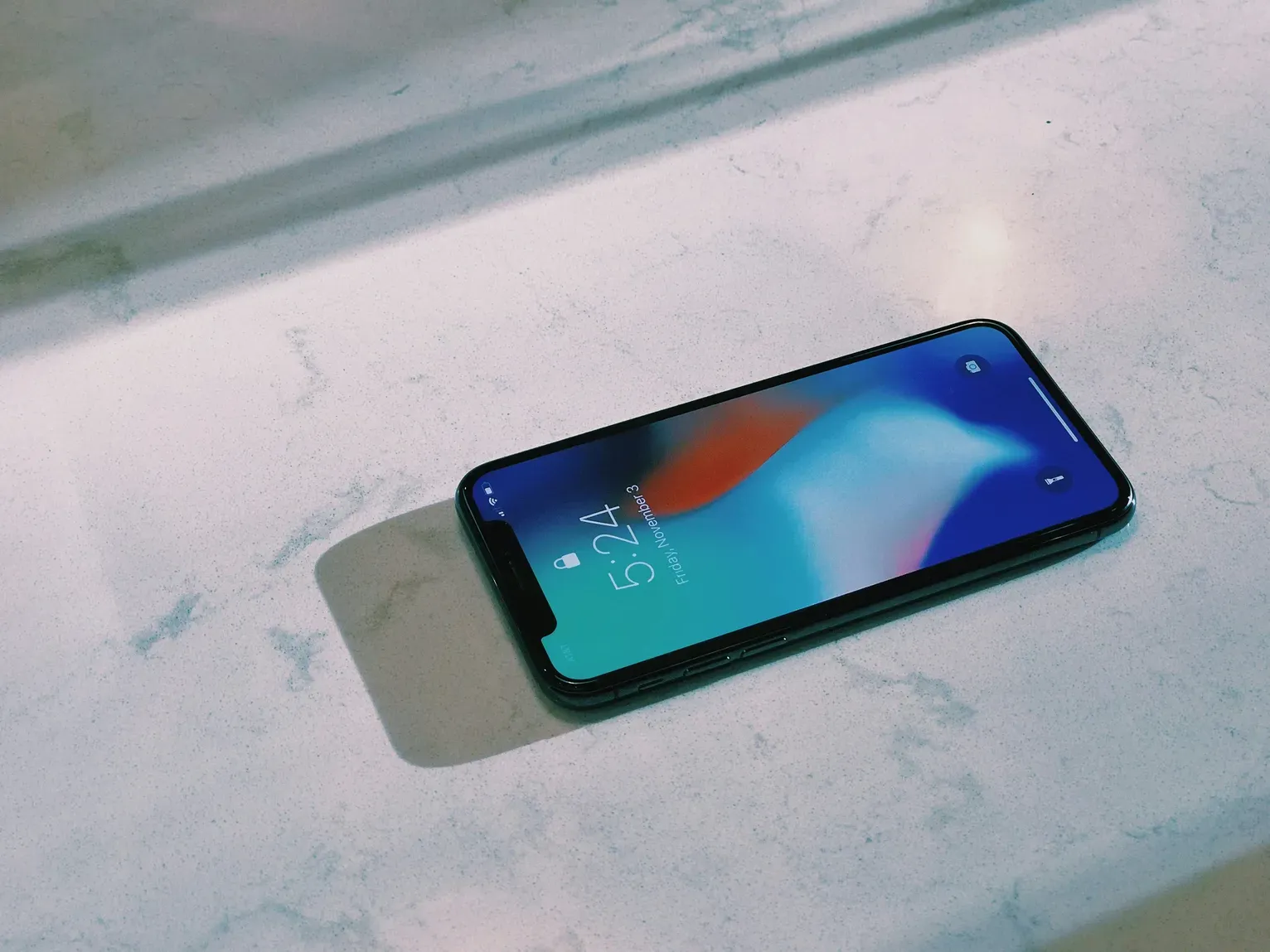 iPhone resting on a light marble surface, displaying lock screen with time and signal icons — representing a device ready for eSIM setup or reset.