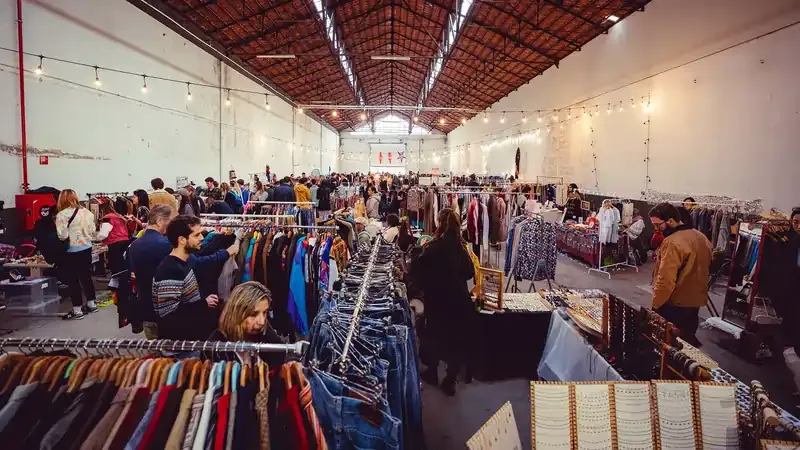 Crowded Lisbon vintage market with people browsing racks of clothes and accessories.