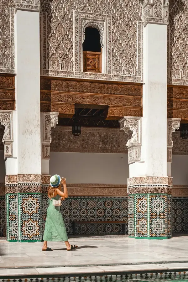 Tourist admiring intricate arches, carved plaster and mosaic tiles in a Moroccan palace.