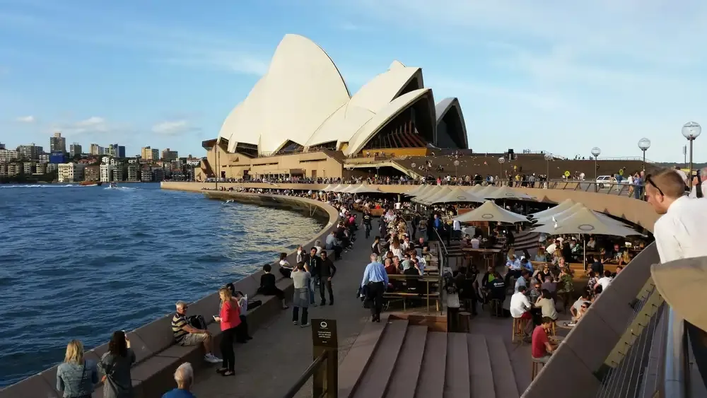 Crowds of people enjoying the waterfront promenade near the Sydney Opera House in Australia,