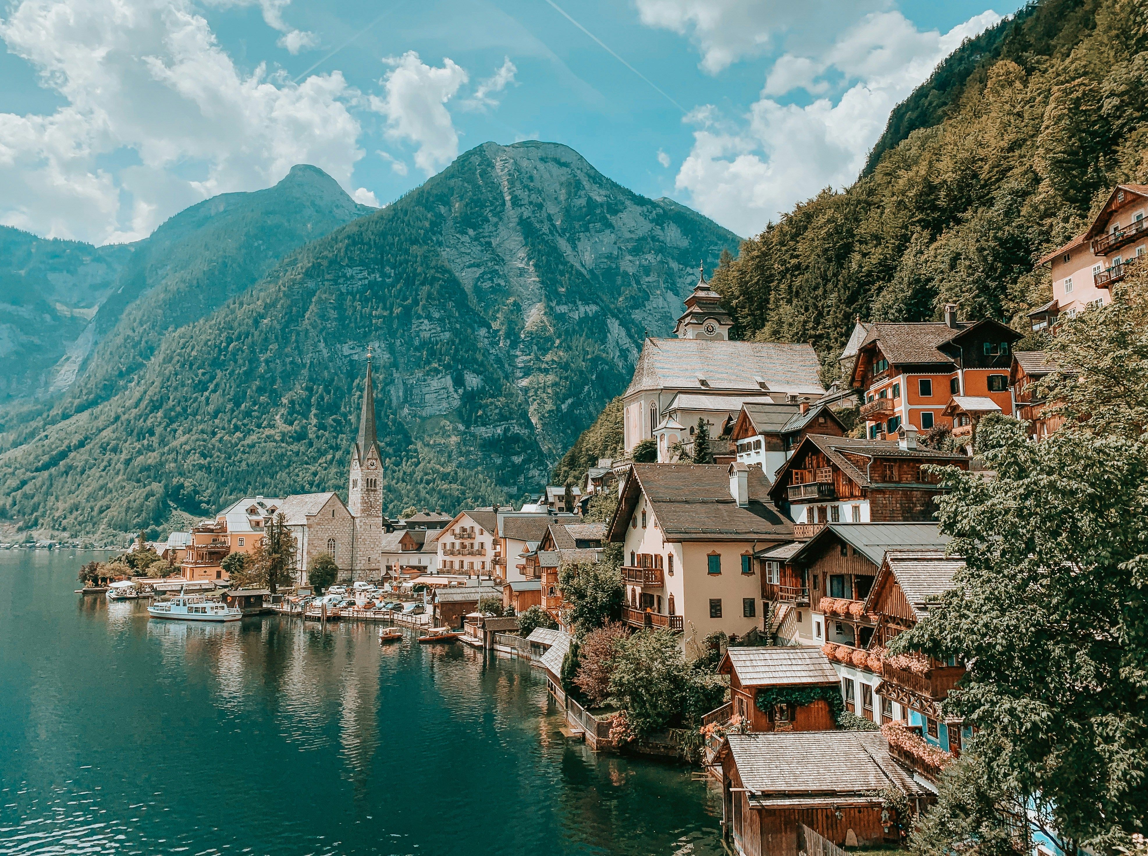 Picturesque view of Hallstatt, Austria — a popular European road trip destination — with alpine houses, a lakeside church, and mountains in the background.