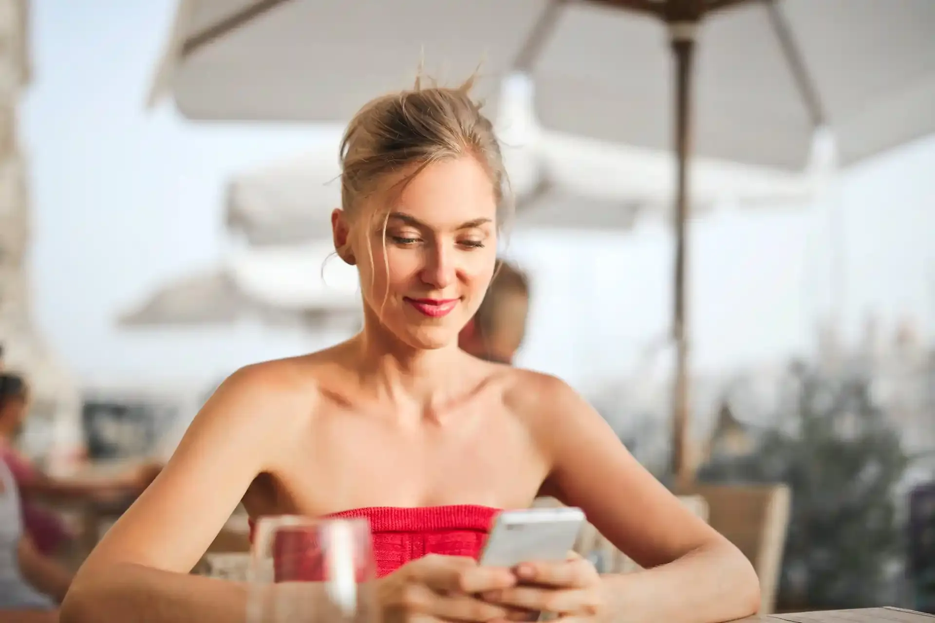 Smiling woman using smartphone at an outdoor café, representing convenient data access abroad with travel eSIM.