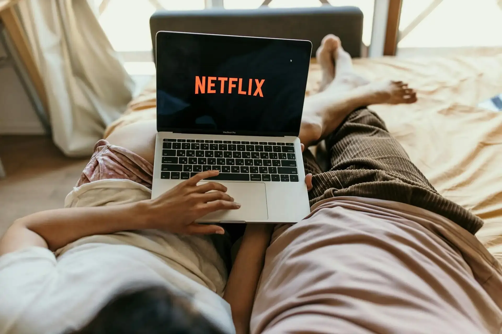 Couple relaxing on a bed while streaming Netflix on a MacBook Pro, illustrating data usage while watching shows on a laptop.