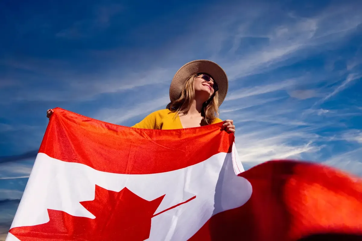 Happy woman holding Canadian flag against a bright blue sky — stay connected while traveling in Canada with a reliable eSIM