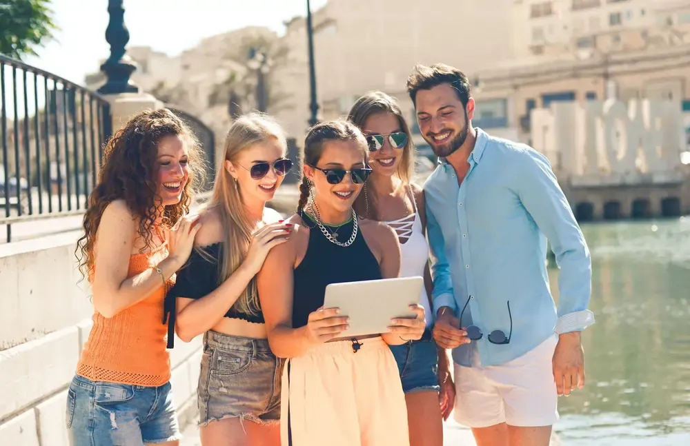 Group of young travelers smiling while looking at a tablet outdoors