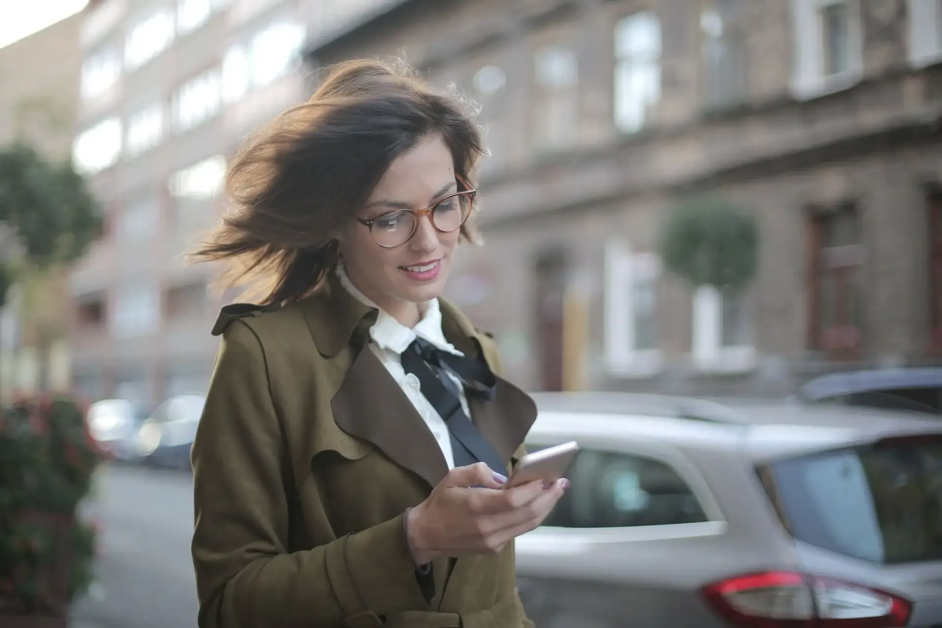 Smiling woman using her phone while walking outdoors.