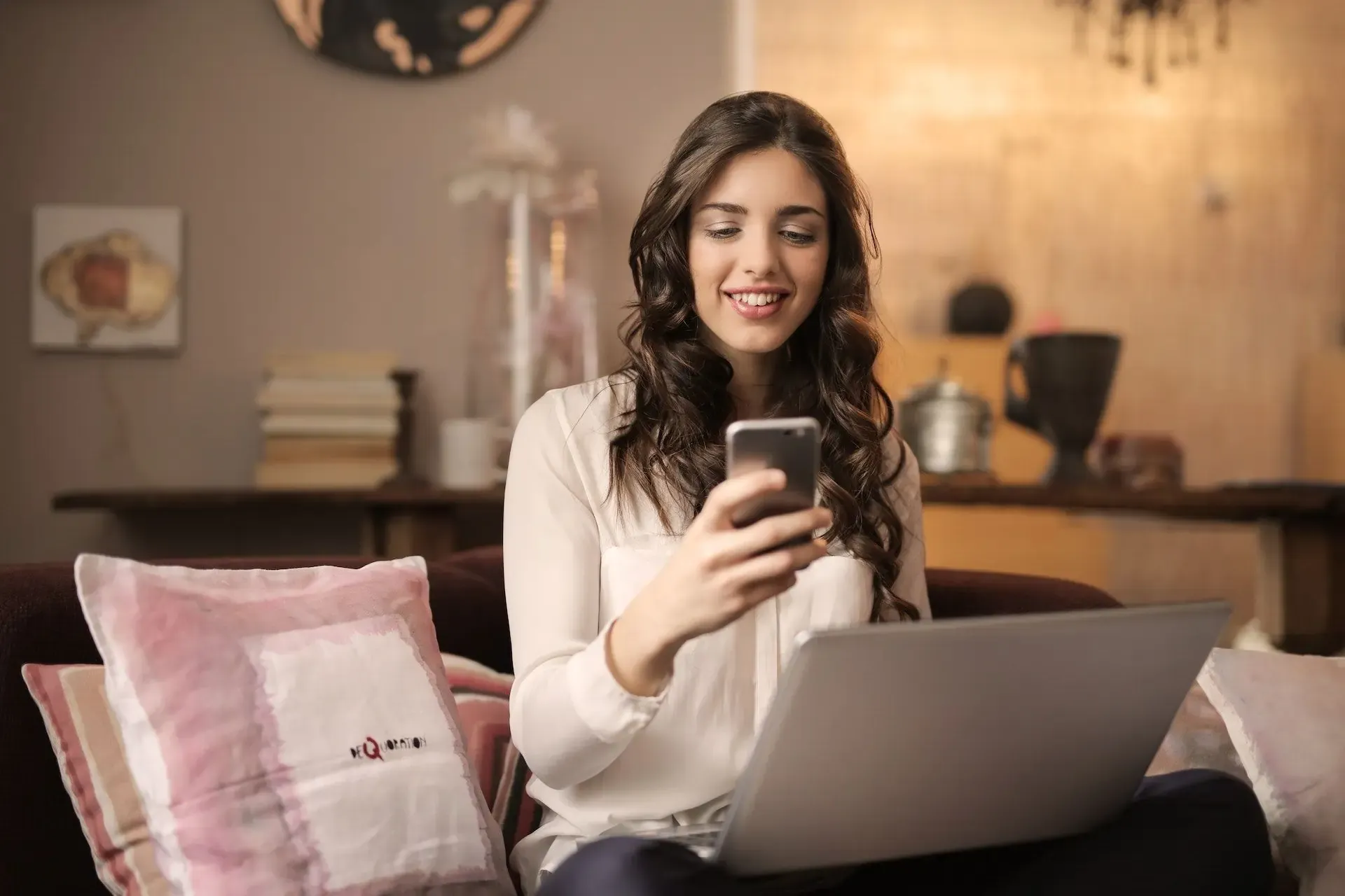 Smiling woman using smartphone and laptop at home
