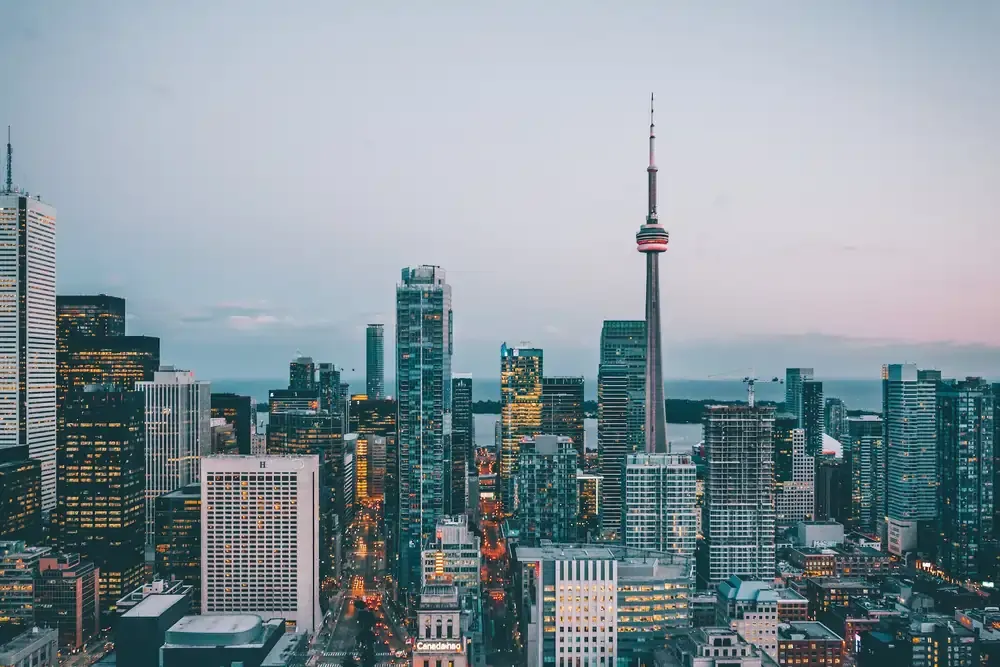 Downtown Toronto skyline at dusk with the CN Tower prominently rising above modern skyscrapers, city lights beginning to illuminate the scene.