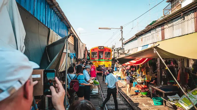 Tourists taking photos of a train passing through the Maeklong Railway Market in Thailand