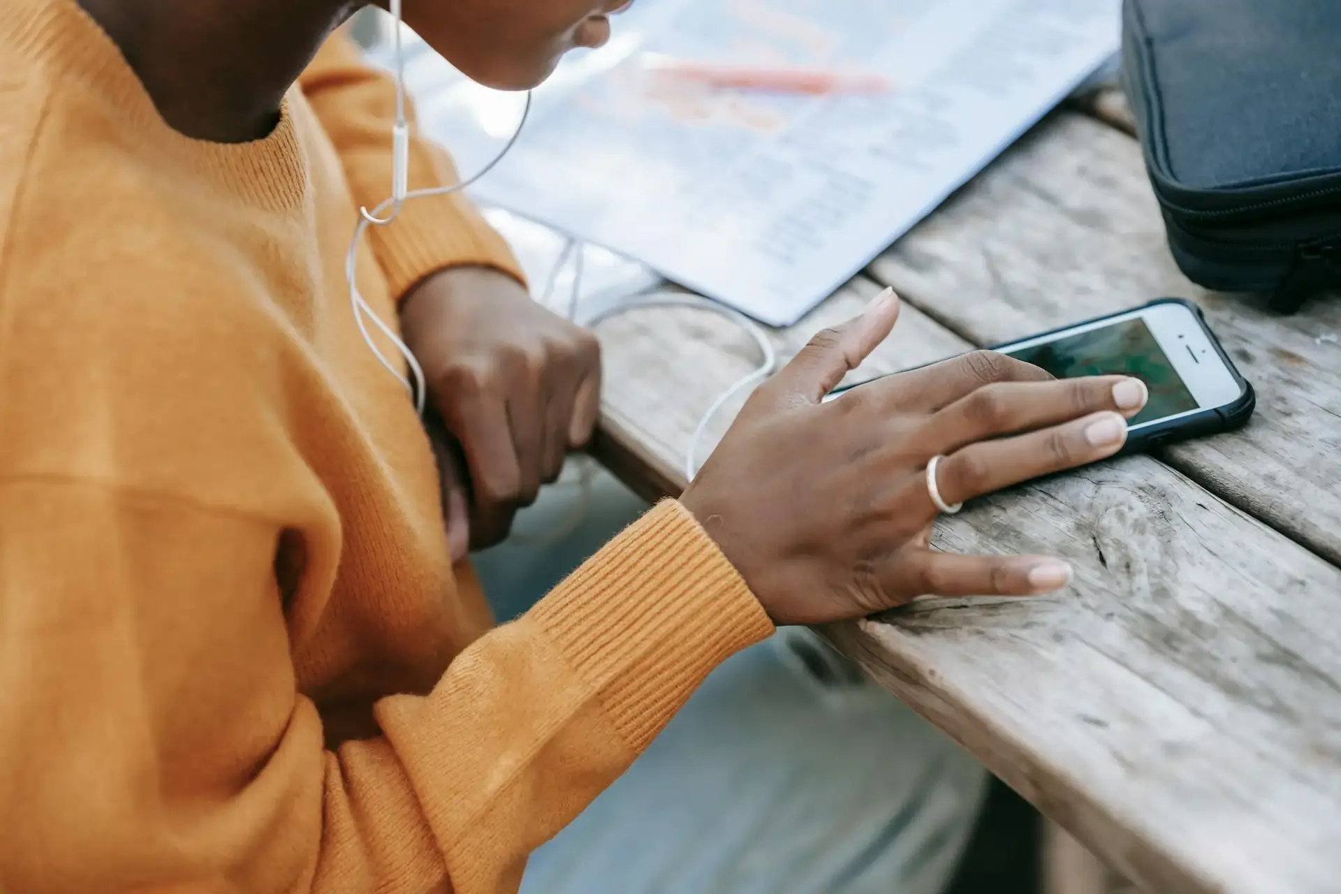 Person using smartphone at a table with earphones plugged in.