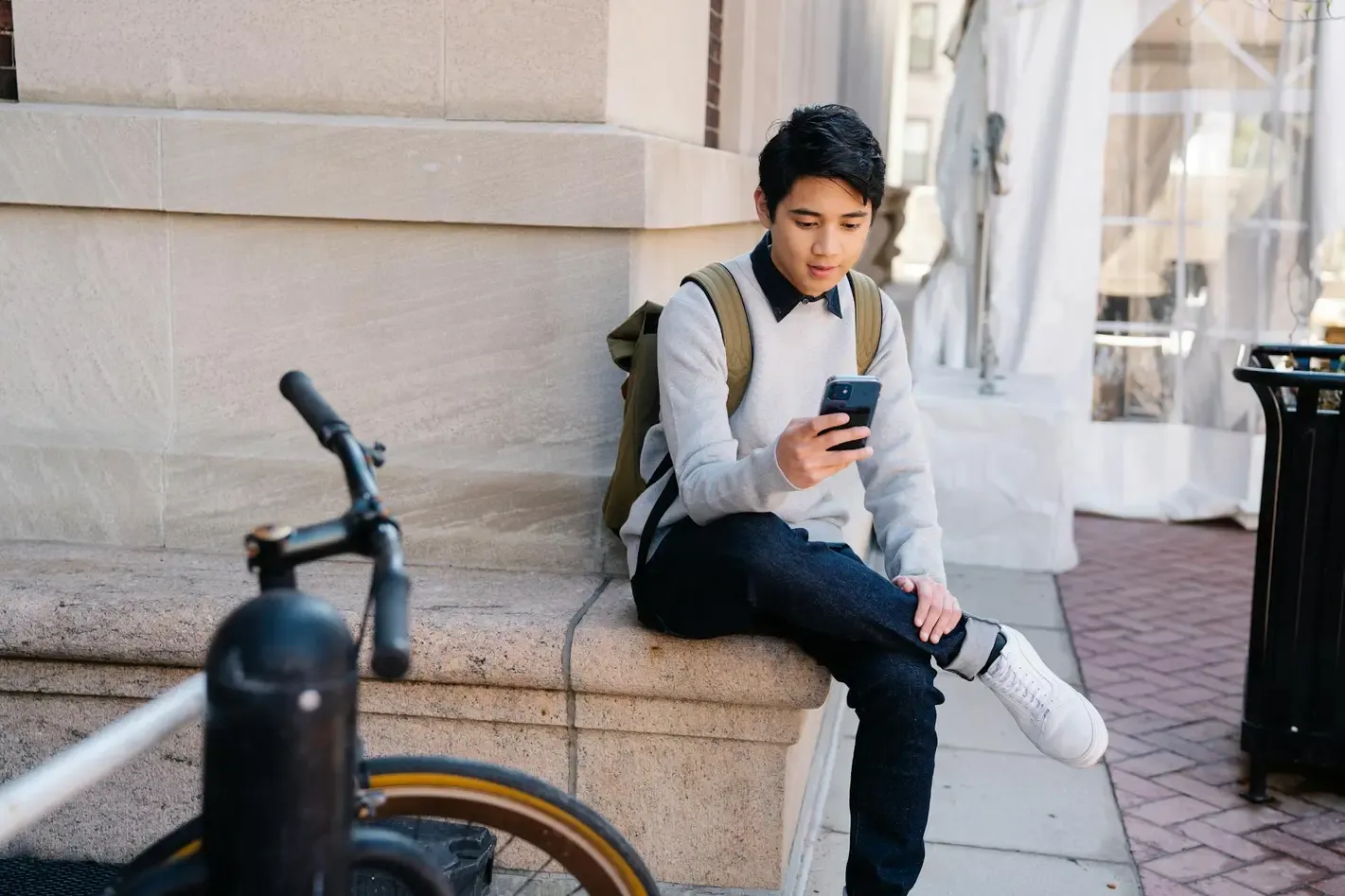 Young man sitting outdoors using his smartphone, representing how SIM cards store essential mobile data like contacts, network information, and SMS messages.