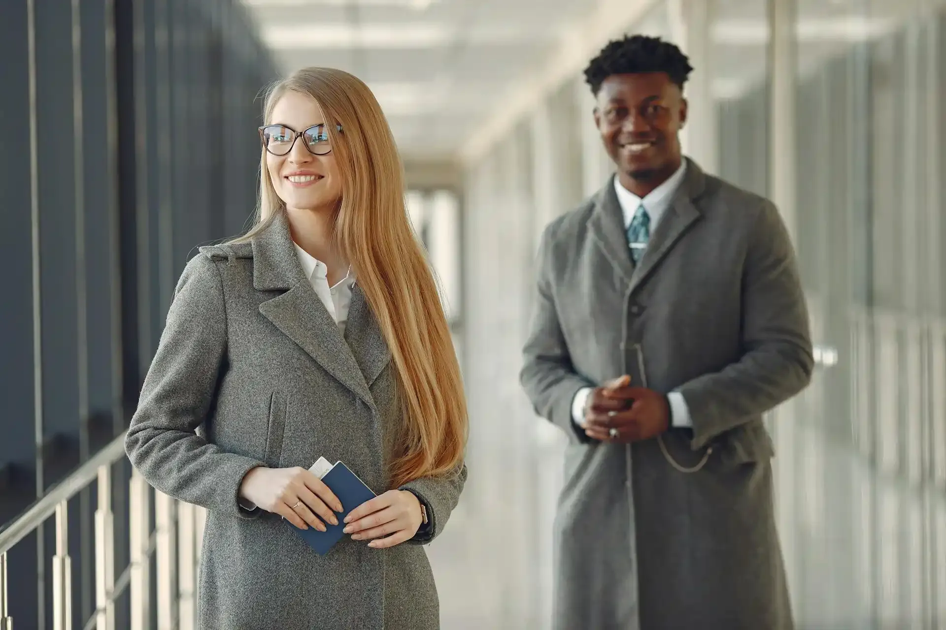 Professionally dressed business travelers holding passports in an airport corridor, highlighting the convenience of eSIMs for seamless corporate travel connectivity.
