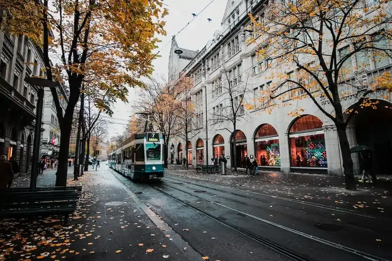 Streetcar in a European city during autumn, surrounded by historic buildings and trees with golden leaves