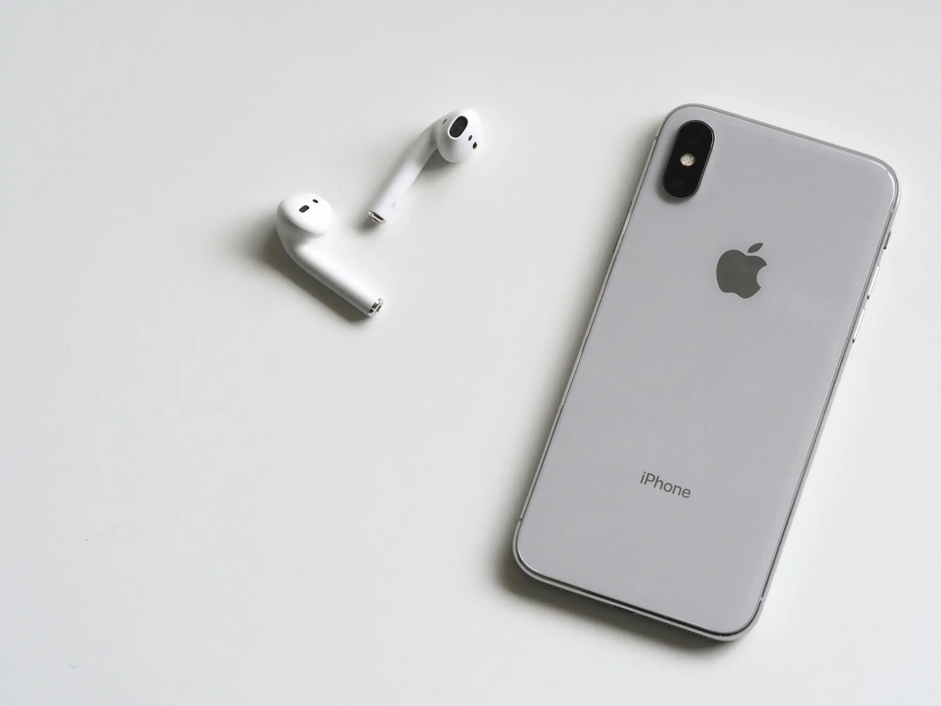 Flat lay of a silver iPhone and a pair of wireless AirPods on a white surface