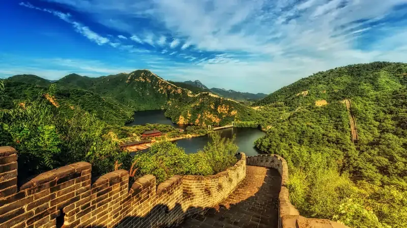 Scenic view of the Great Wall of China winding through lush green mountains under a vibrant blue sky