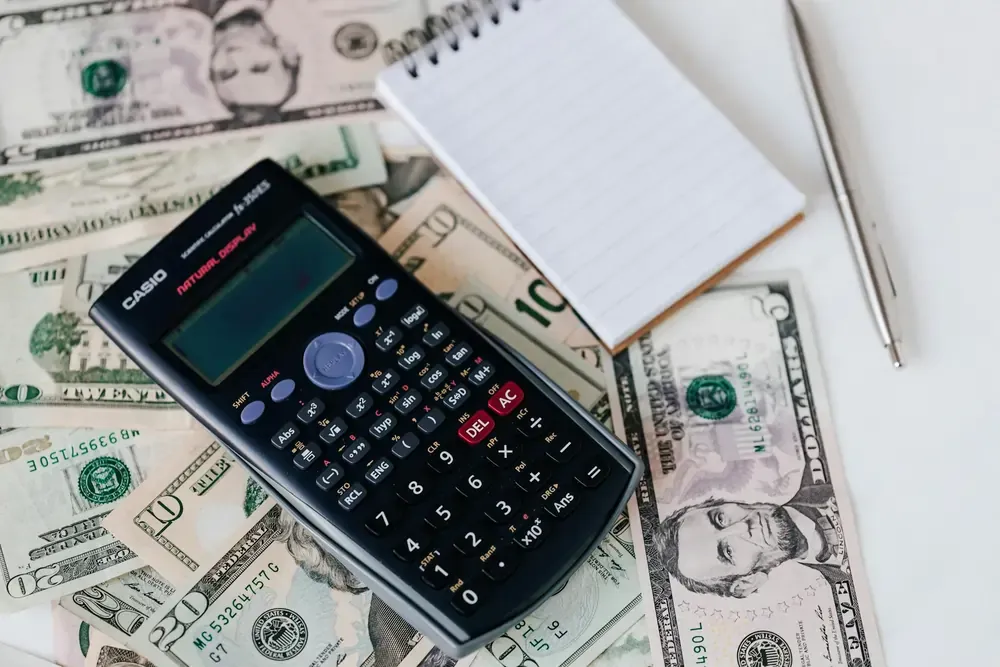 Close-up of a calculator on top of US dollar bills, next to a notepad and pen