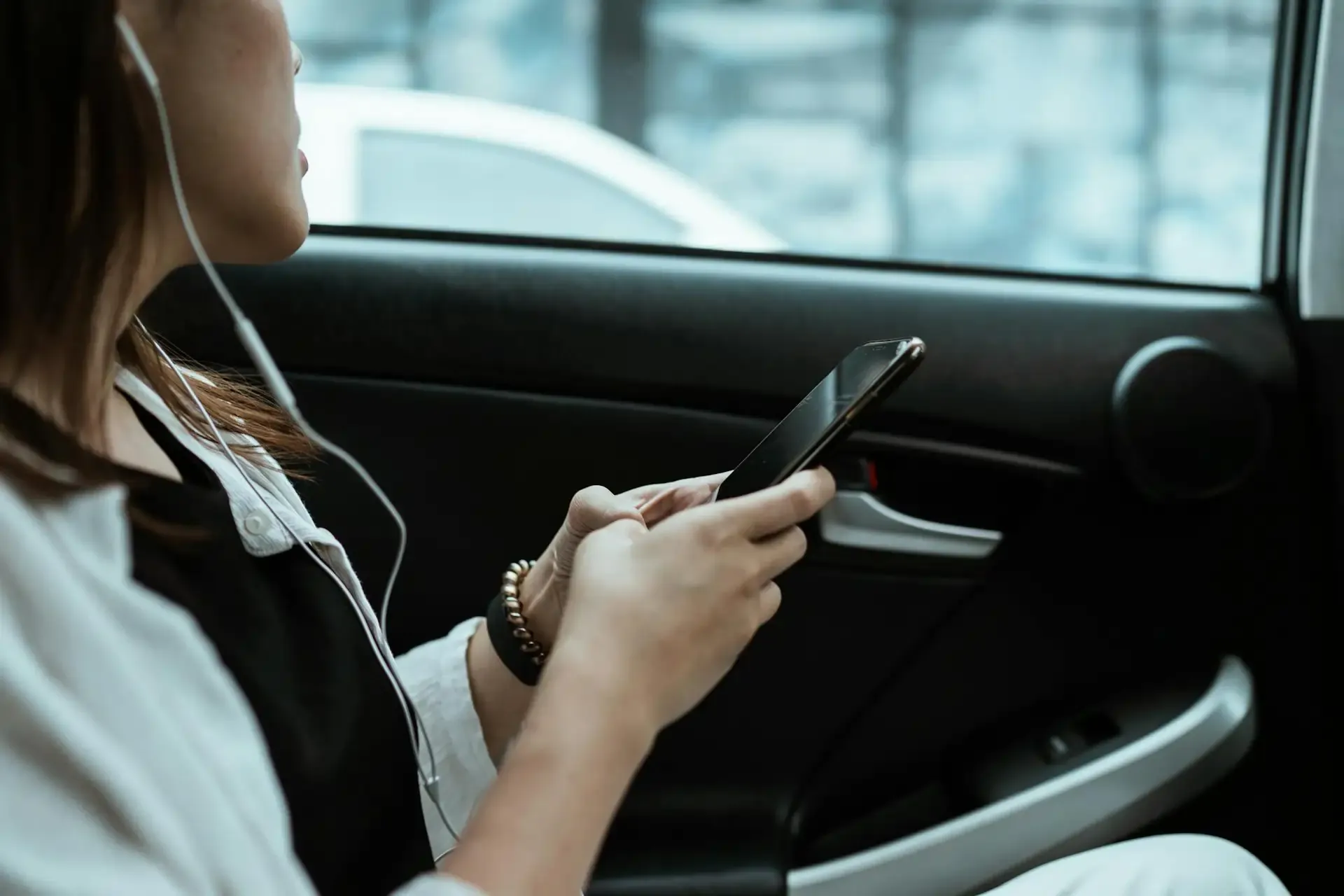 Woman in a taxi using her phone with earphones, illustrating how to fix international roaming not working while traveling.