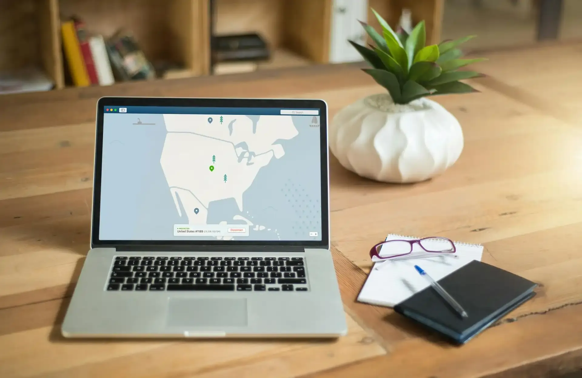 Open laptop on a wooden table with a VPN dashboard on screen, glasses and pen nearby—illustrating using a VPN for secure travel internet.