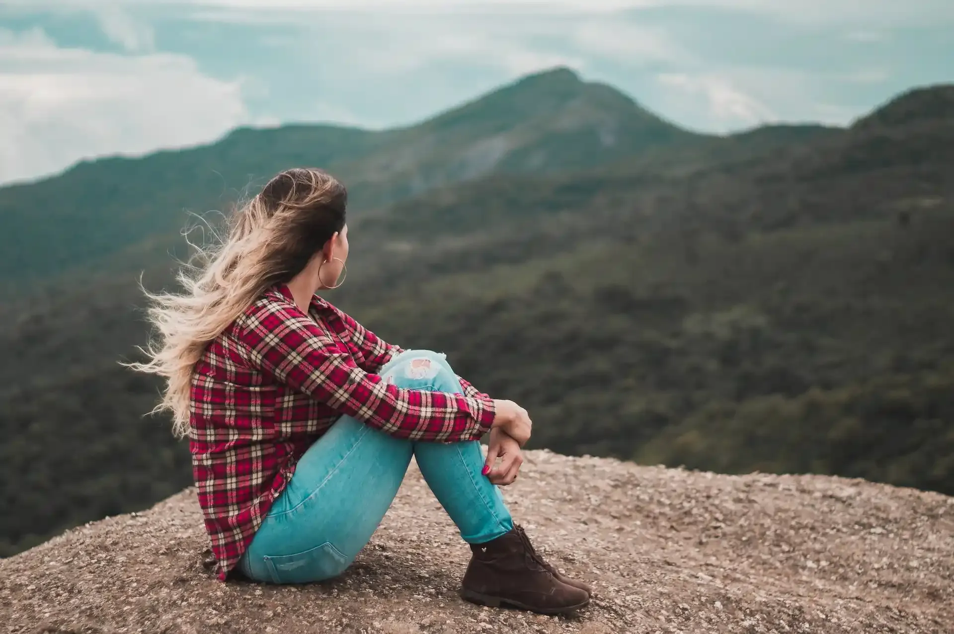 Woman sitting on a mountain overlook, contemplating factors for choosing the best travel SIM card.