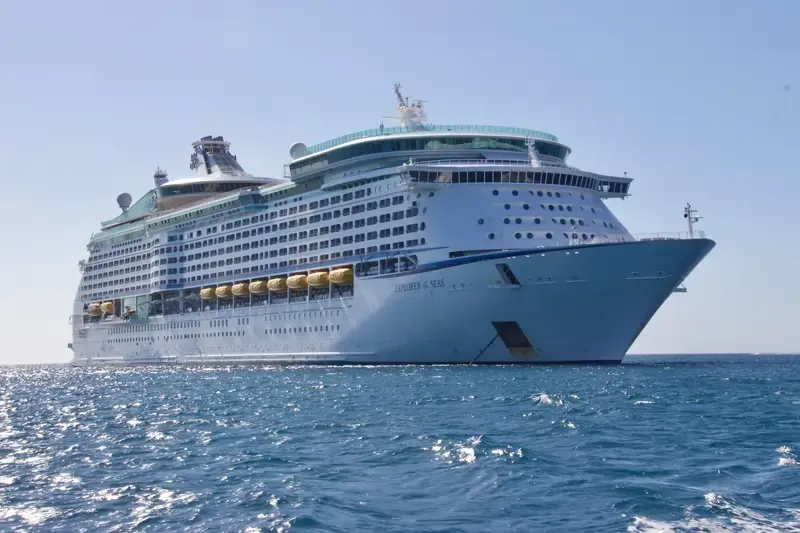 A large cruise ship sails across open waters under a clear blue sky