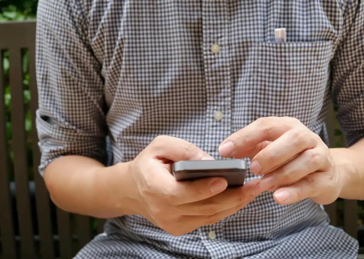 Man in checkered shirt using smartphone outdoors.